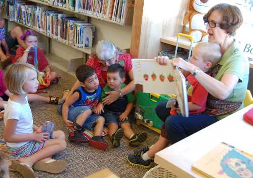 Marcine Crowhurst reads to an enthusiastic preschool group at the new Middletown Library in Middletown, Calif., as part of the 2013 Children's Summer Reading Program. From left to right, Hadley Brown, 5; Diego Pimentel, 3, and Benjamin Pimentel, 2, sitting with Patty Buck; and David Britton. Photo by John Lindblom. mtownlibrarykidsreading