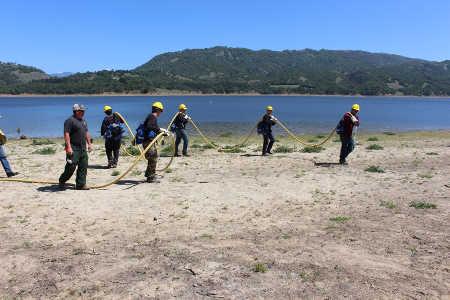 Crewmember Bryan Stencil sprays water as fellow Willits Organized Crewmembers follow behind to safely lay a fire-hose line along Lake Mendocino near Ukiah, Calif., on Thursday, April 17, 2014. Photo courtesy of the Mendocino National Forest. 041714willitscrew2