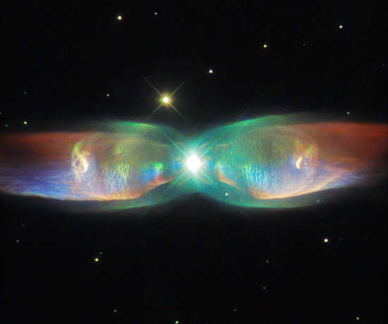 The shimmering colors visible in this NASA/ESA Hubble Space Telescope image show off the remarkable complexity of the Twin Jet Nebula. The new image highlights the nebula’s shells and its knots of expanding gas in striking detail. Two iridescent lobes of material stretch outwards from a central star system. Within these lobes two huge jets of gas are streaming from the star system at speeds in excess of one million kilometers per hour. twinjetnebula